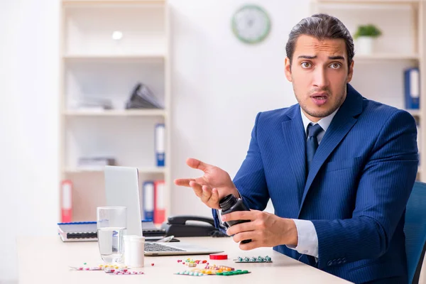 Jonge mannelijke werknemer en veel pillen op het bureau — Stockfoto