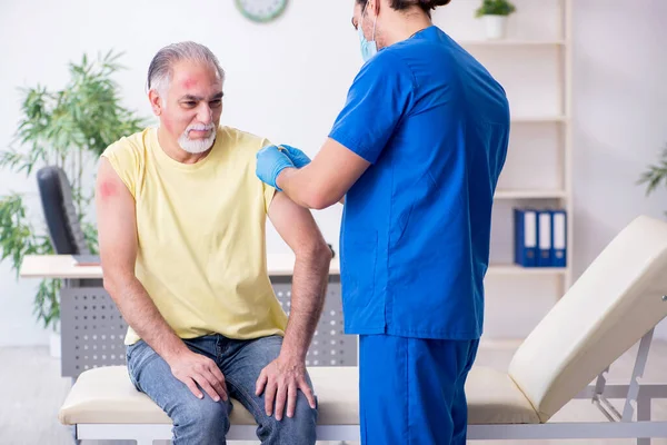 Verwondde oude man op bezoek bij jonge mannelijke arts traumatoloog — Stockfoto