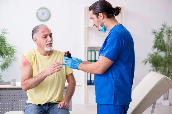 Yaralı yaşlı adam genç erkek doktor travmatoloğu ziyaret ediyor. — Stok fotoğraf