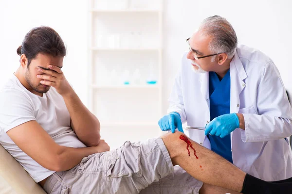 Leg injured man visiting old doctor in first aid concept — Stockfoto