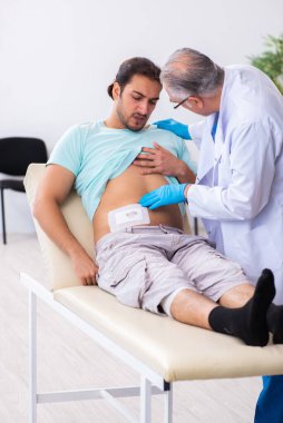 Yaralı genç adam deneyimli erkek doktoru ziyaret ediyor.