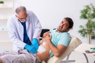Yaralı genç adam deneyimli erkek doktoru ziyaret ediyor.