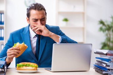 Genç erkek çalışan işyerinde kahvaltı yapıyor.