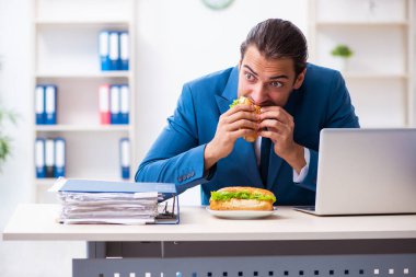 Genç erkek çalışan işyerinde kahvaltı yapıyor.