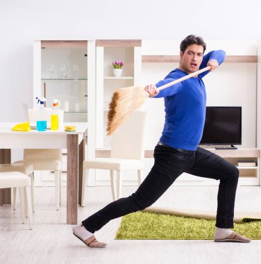 Genç adam yerleri süpürgeyle temizliyor.