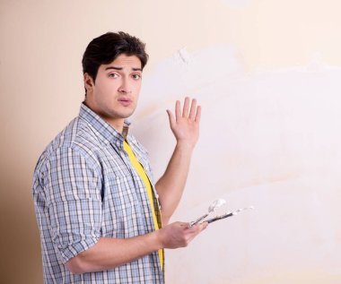 Evdeki duvara alçı yapıştıran genç adam.