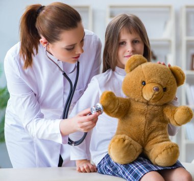 Kadın doktor oyuncak ayıyla küçük tatlı kızı muayene ediyor.