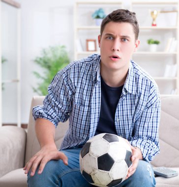 Evde futbol izleyen genç bir öğrenci.