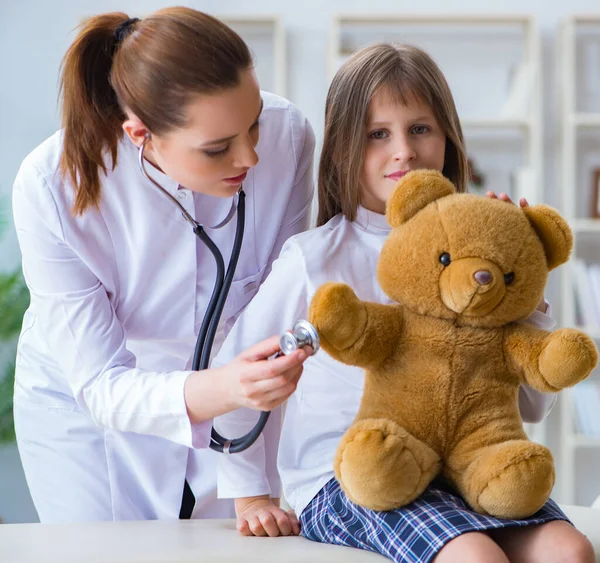 Mujer médico femenino examinando poco linda chica con juguete oso — Foto de Stock