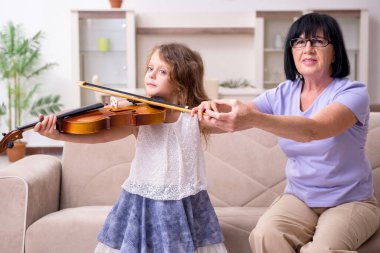 Yaşlı kadın küçük kıza keman çalmayı öğretiyor.
