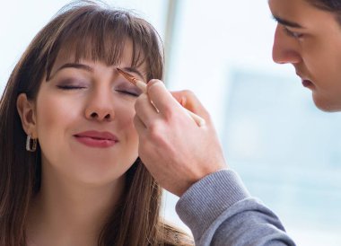 Güzellik salonunda güzel bir kadın için makyaj yapan adam.