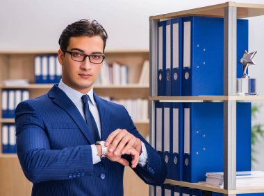 Dosyalarla rafın yanında duran genç adam.