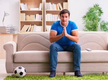 Evdeki kanepede oturup futbol izleyen bir adam.