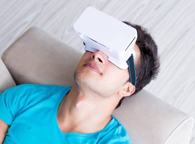 VR gözlüklü genç adam kanepede dinleniyor.