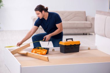 Genç erkek müteahhit eve mobilya kuruyor.