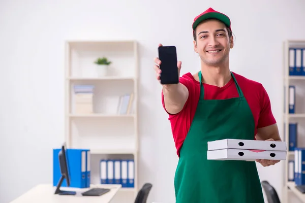 Jonge mannelijke koerier die pizza aflevert op kantoor — Stockfoto