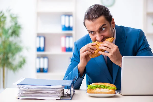 Ung manlig anställd som äter frukost på arbetsplatsen — Stockfoto