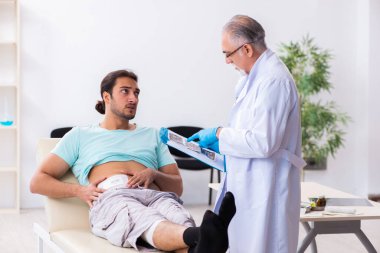 Yaralı genç adam deneyimli erkek doktoru ziyaret ediyor.