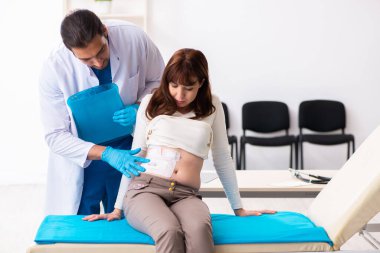 Yaralı genç kadın genç erkek doktoru ziyaret ediyor.