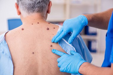 Yaşlı adam genç erkek doktor dermatoloğu ziyaret ediyor.