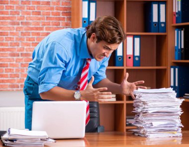 Ofiste aşırı işi olan genç bir çalışan oturuyor.