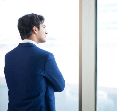 Genç yakışıklı işadamı pencerede duruyor.