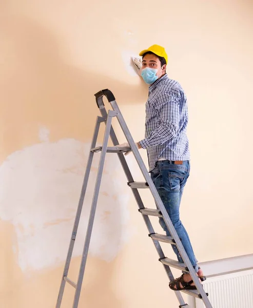 Jonge aannemer schuurt muur af met schuurpapier — Stockfoto