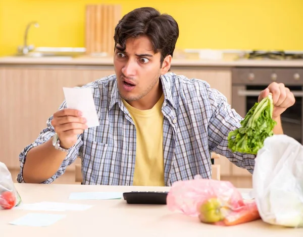 Молодой человек рассчитывает расходы на овощи на кухне — стоковое фото
