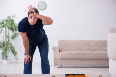 Genç erkek müteahhit eve mobilya kuruyor.