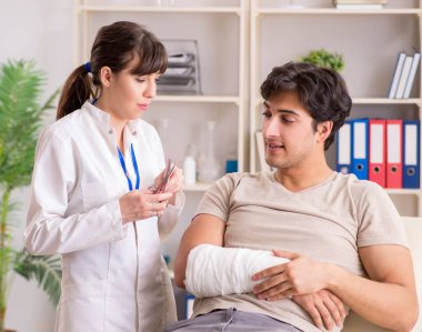 Kolu bandajlı genç adam kadın doktor travmatologunu ziyaret ediyor.