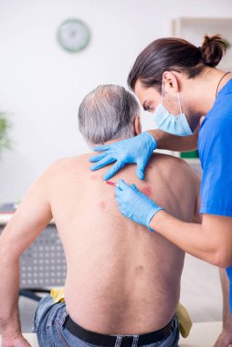 Yaşlı adam genç erkek doktor dermatoloğu ziyaret ediyor.