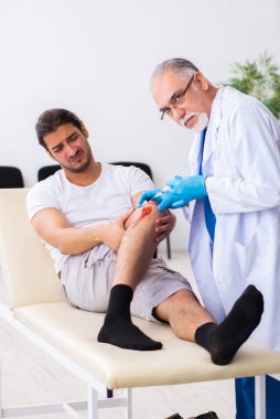 Yaralı adam ilk yardım konseptinde yaşlı doktoru ziyaret ediyor.