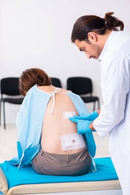 Yaralı genç kadın genç erkek doktoru ziyaret ediyor.