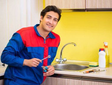 Tesisatçı mutfakta musluğu tamir ediyor.