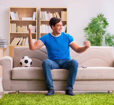Evdeki kanepede oturup futbol izleyen bir adam.