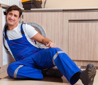 Tamirci mutfakta çamaşır makinesini tamir ediyor.