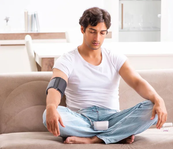 Hombre joven midiendo la presión arterial en casa — Foto de Stock