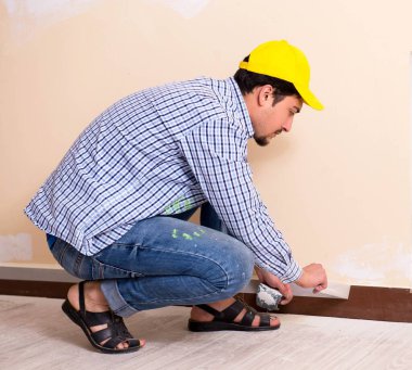 Genç müteahhit zımpara kağıdıyla duvarı zımparalıyor.