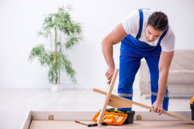 Genç erkek müteahhit eve mobilya kuruyor.