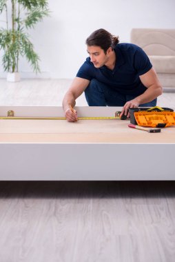 Genç erkek müteahhit eve mobilya kuruyor.