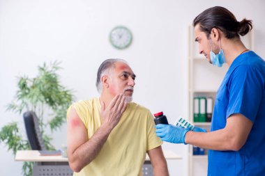 Yaralı yaşlı adam genç erkek doktor travmatoloğu ziyaret ediyor.