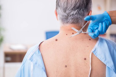 Yaşlı adam genç erkek doktor dermatoloğu ziyaret ediyor.