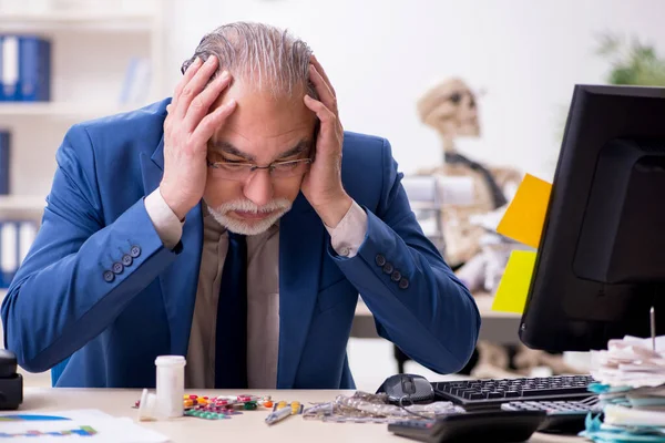 Old male sick employee working overtime in the office