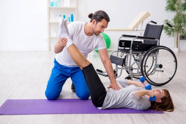 Tekerlekli sandalyedeki kadın kişisel koçuyla spor egzersizleri yapıyor.