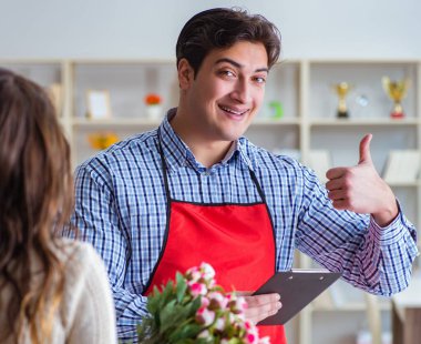 Çiçekçi yardımcısı kadın müşteriye çiçek satıyor.