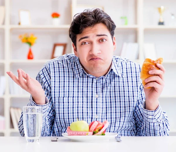 El hombre tiene un dilema entre la comida sana y el pan en la dieta con —  Fotos de Stock