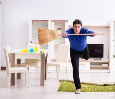 Genç adam yerleri süpürgeyle temizliyor.