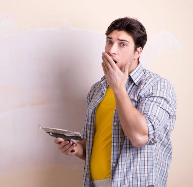 Evdeki duvara alçı yapıştıran genç adam.