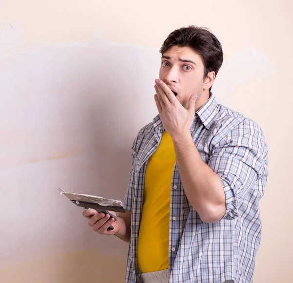 Evdeki duvara alçı yapıştıran genç adam.