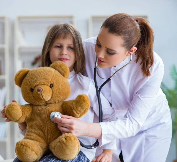 Vrouw vrouwelijke arts onderzoeken klein schattig meisje met speelgoed beer — Stockfoto